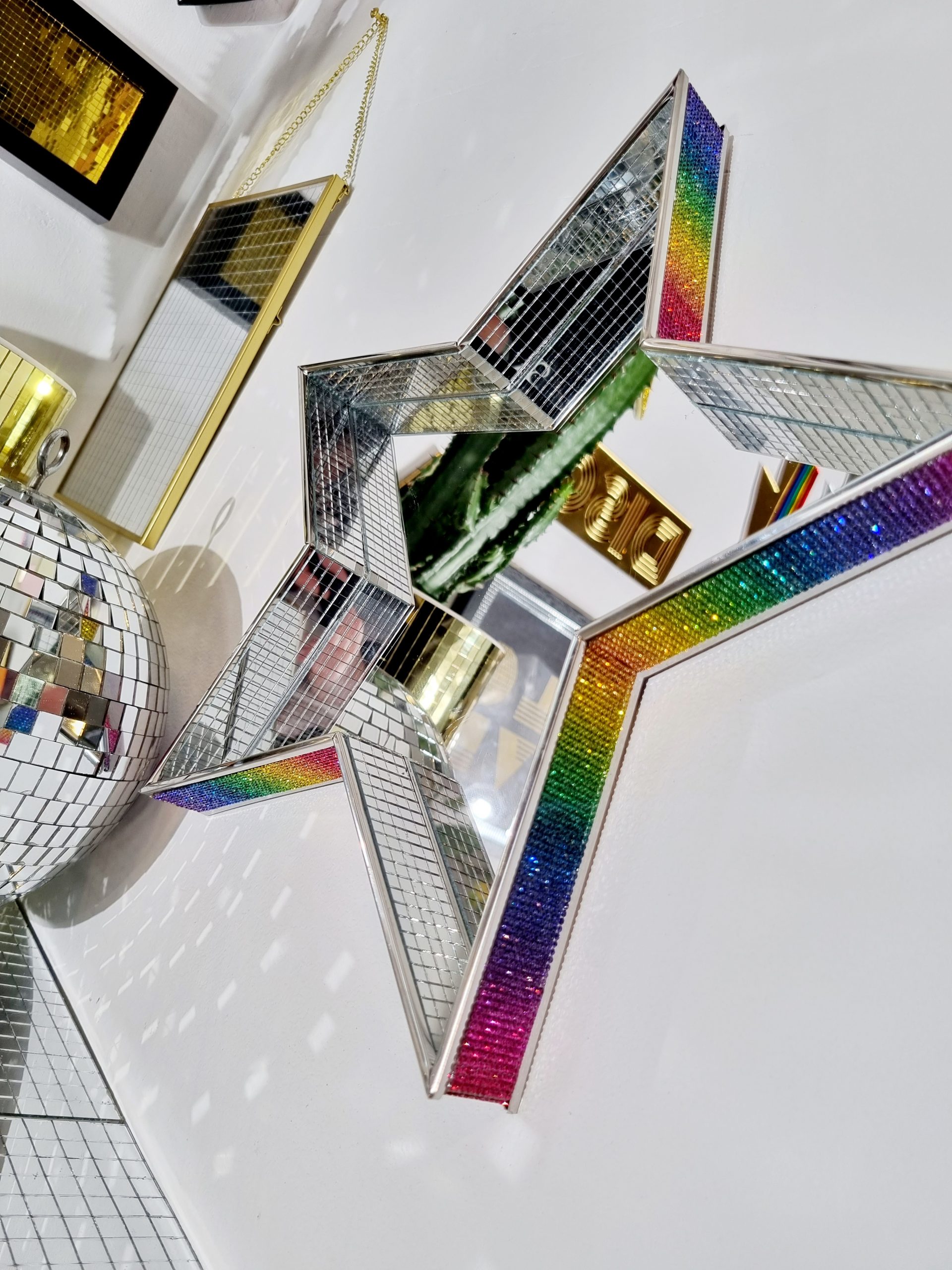 A MIRROR IN THE SHAPE OF A STAR, EDGED WITH DISCO MIRROR TILES AND RAINBOW RHINESTONES.