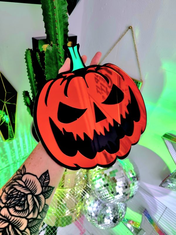 A mirror in the design of a pumpkin. It has a black base layered with gold mirror and a green mirror stalk.