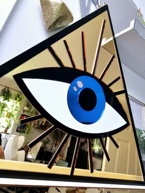 A mirror in the shape of an all seeing eye. The mirror is a gold triangle with an eye in the middle.