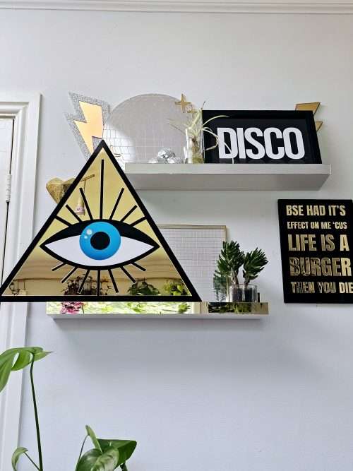 A mirror in the shape of an all seeing eye. The mirror is a gold triangle with an eye in the middle.