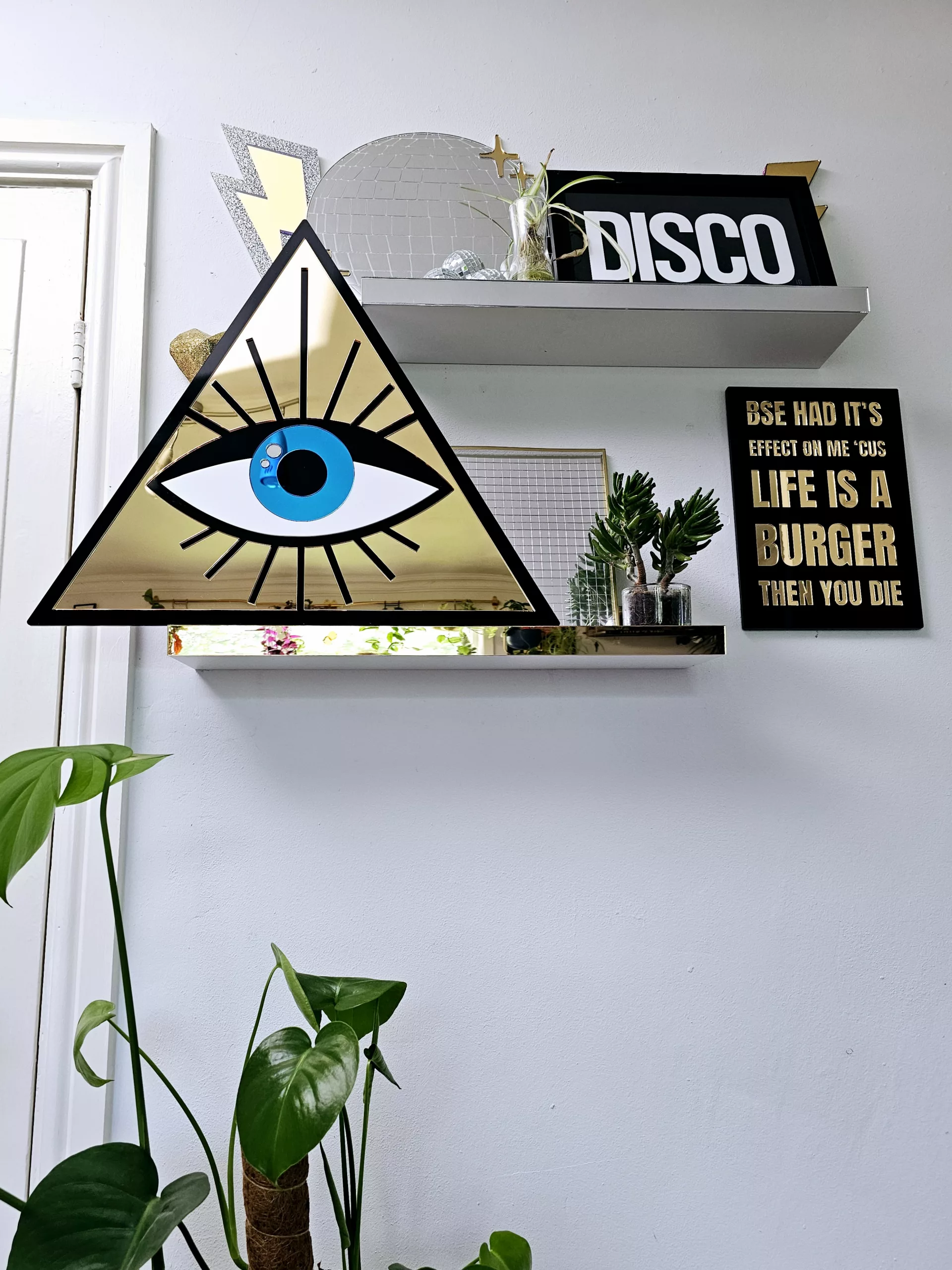 A mirror in the shape of an all seeing eye. The mirror is a gold triangle with an eye in the middle.