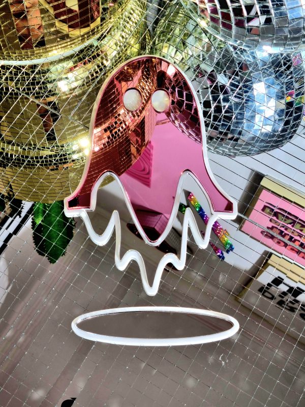 Acrylic wall art in the shape of a ghost. The piece is made from gloss white, and silver and pink mirror acrylic. The piece is sitting flat against a some disco mirror tiles.