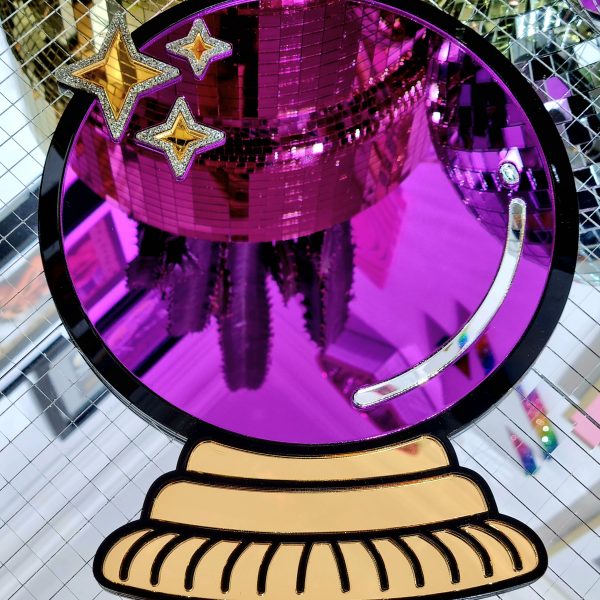 A handmade mirror in the shape of a crystal ball. The design has a black outline with gold mirror stand and purple mirror crystal ball.