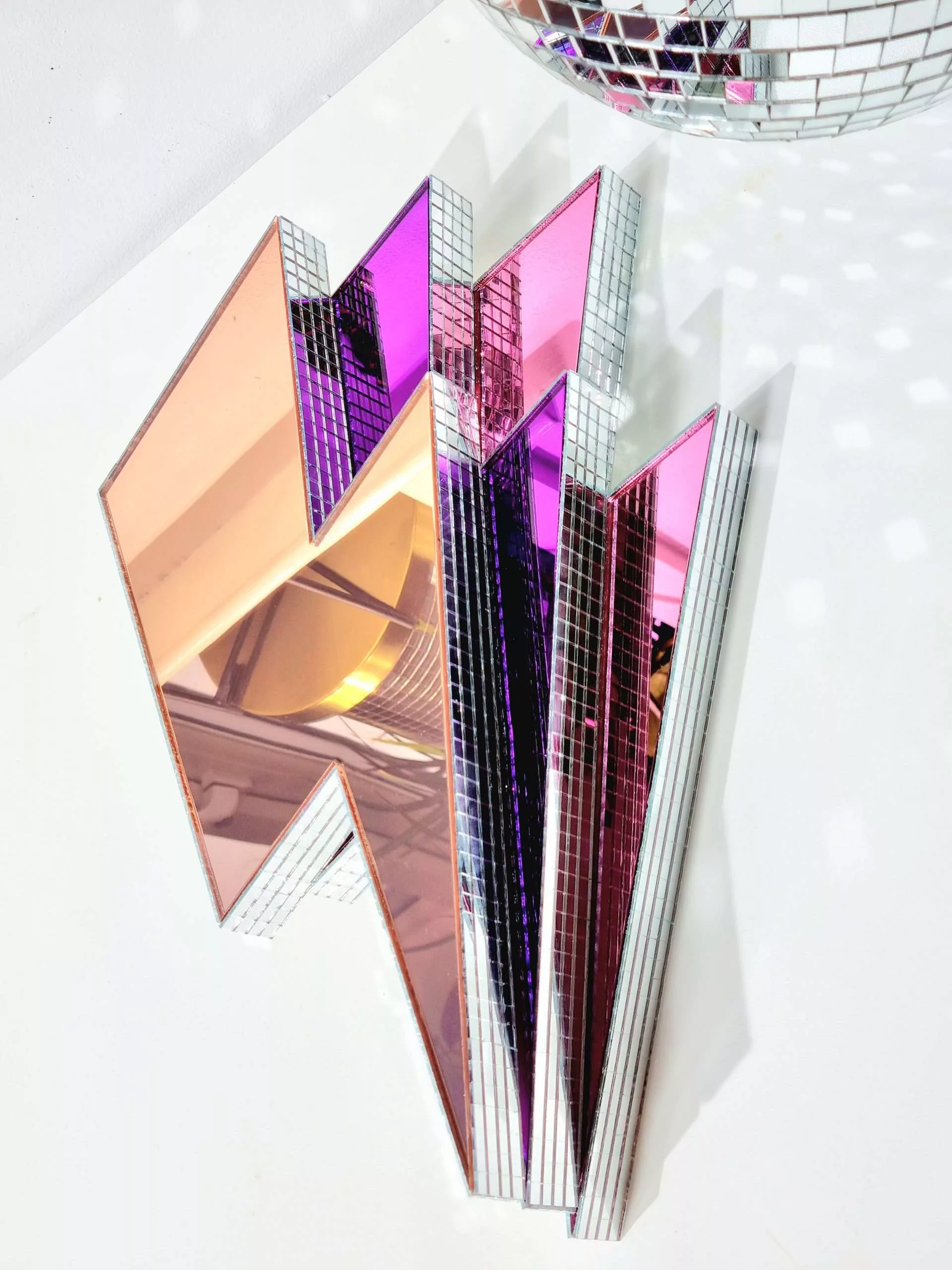 Handmade mirror lightning bolts in pink, purple and rose gold on a white background.