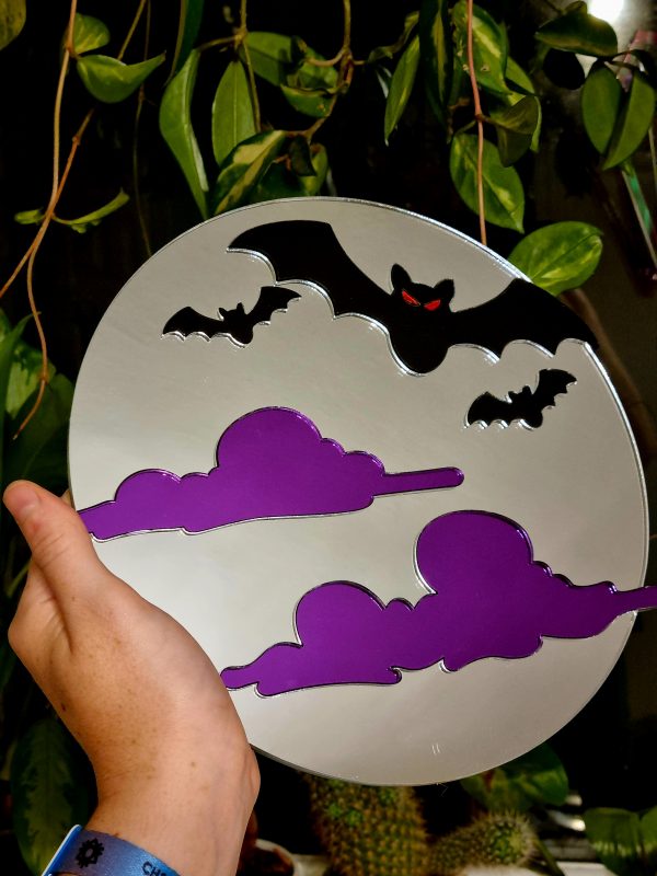 A mirror in the shape of a moon with black bats and purple clouds trailing across it.