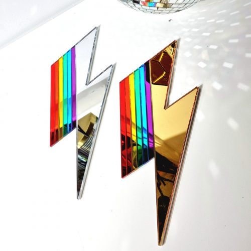 A handmade mirror in the shape of a lightning bolt. Most of the bolt is silver, with strips representing each colour of the rainbow.