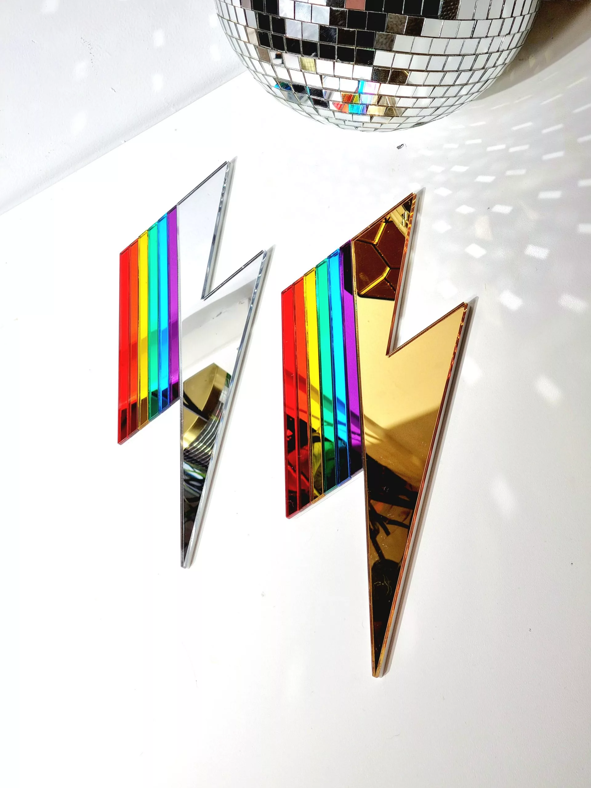 A handmade mirror in the shape of a lightning bolt. Most of the bolt is silver, with strips representing each colour of the rainbow.