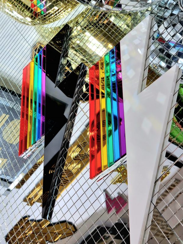 Two pieces of wall art in the shape of lightning bolts. Each has either a white or black gloss base, accented with pieces or rainbow coloured mirror.