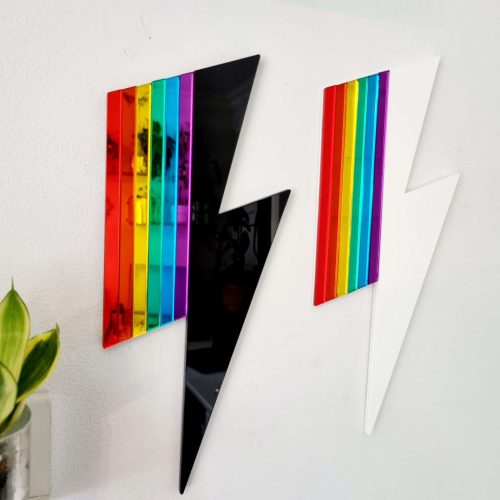 Two pieces of wall art in the shape of lightning bolts. Each has either a white or black gloss base, accented with pieces or rainbow coloured mirror.