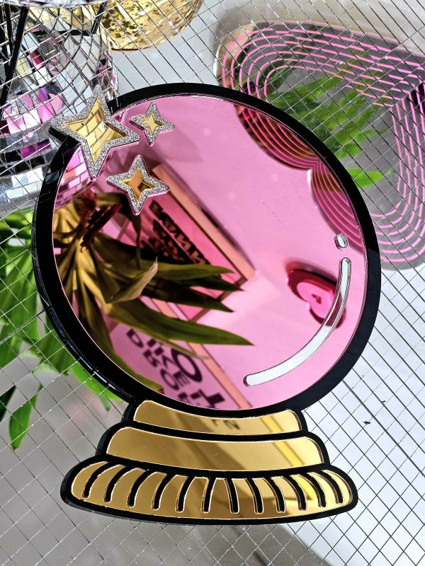 A handmade mirror in the shape of a cryatsl ball. The ball is pink with a black outline and gold details.