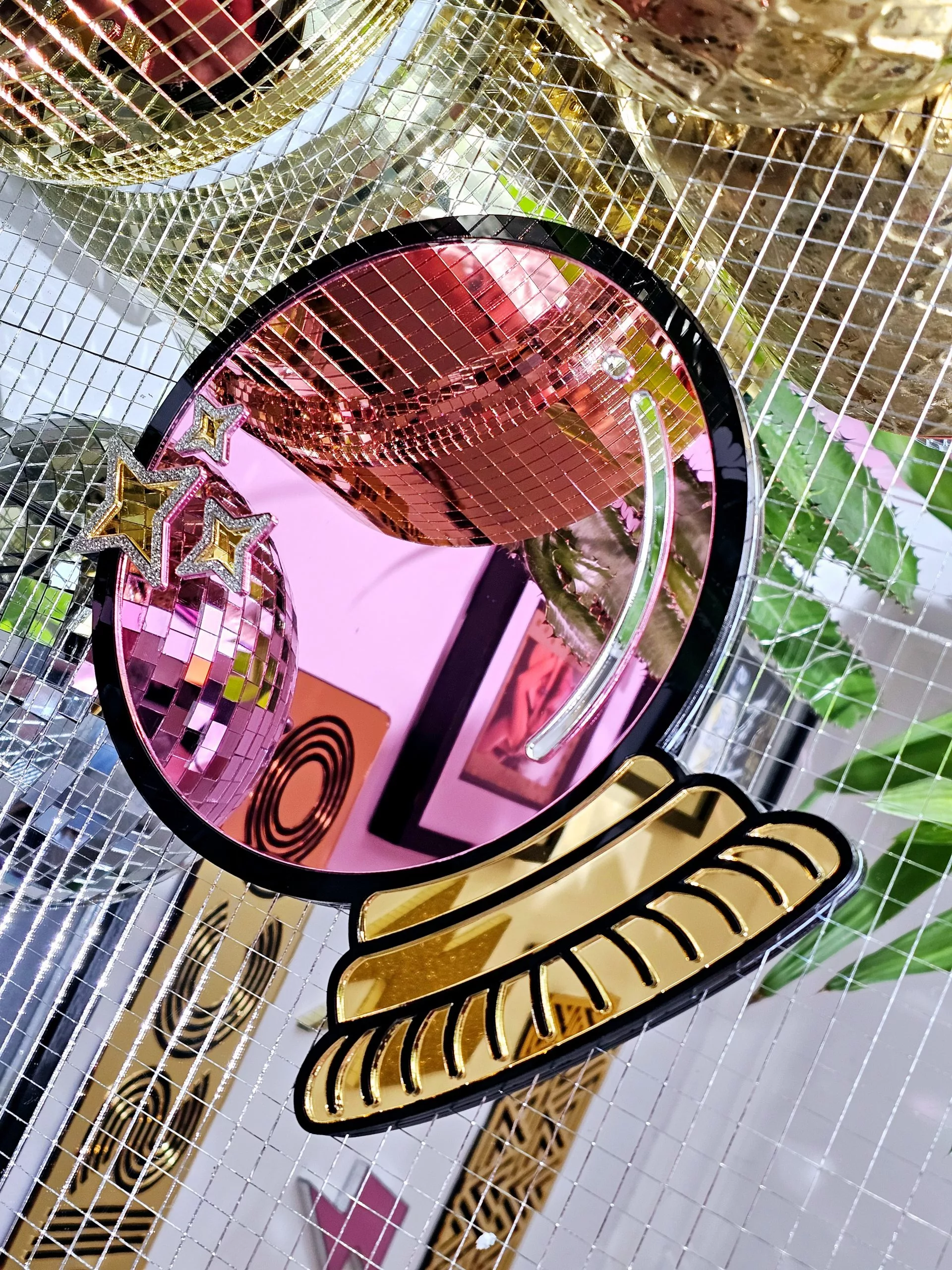A handmade mirror in the shape of a cryatsl ball. The ball is pink with a black outline and gold details.