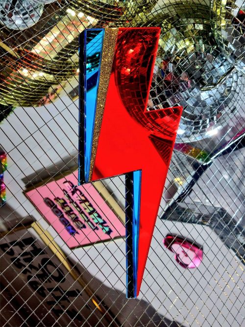 A handmade mirror in the style of the Aladdin Sane David Bowie lghtning bolt. The bolt is made from red and blue mirror with a flash of gold glitter.