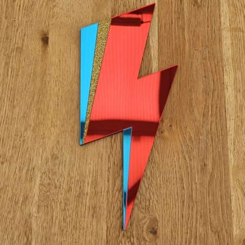 A handmade mirror in the style of the Aladdin Sane David Bowie lghtning bolt. The bolt is made from red and blue mirror with a flash of gold glitter.