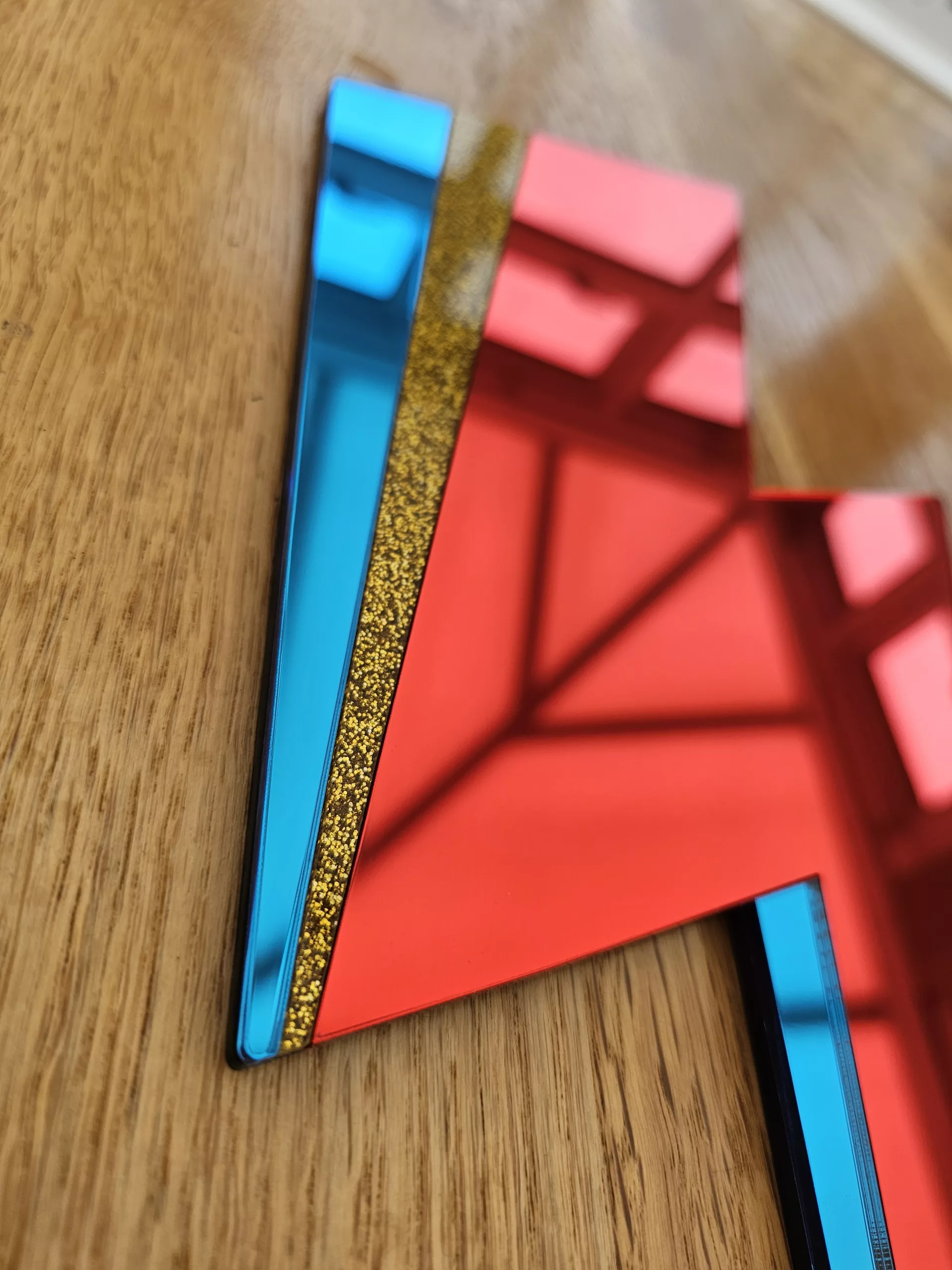 A handmade mirror in the style of the Aladdin Sane David Bowie lghtning bolt. The bolt is made from red and blue mirror with a flash of gold glitter.