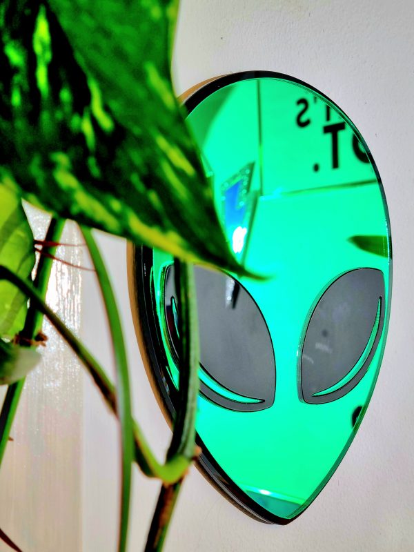 A mirror in the shape of an alien head. The face of the alien is green mirror, with a black gloss outline and black gloss eyes.