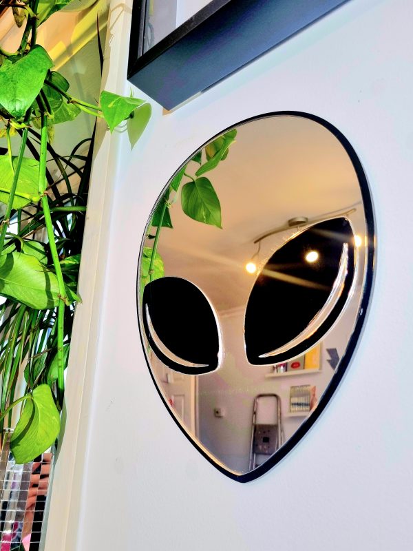 A mirror in the shape of an alien head. The face of the alien is silver mirror, with a black gloss outline and black gloss eyes.