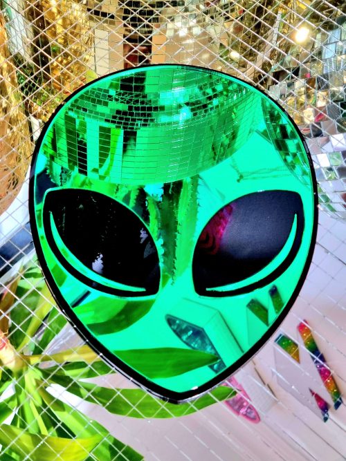 A mirror in the shape of an alien head. The face of the alien is green mirror, with a black gloss outline and black gloss eyes.