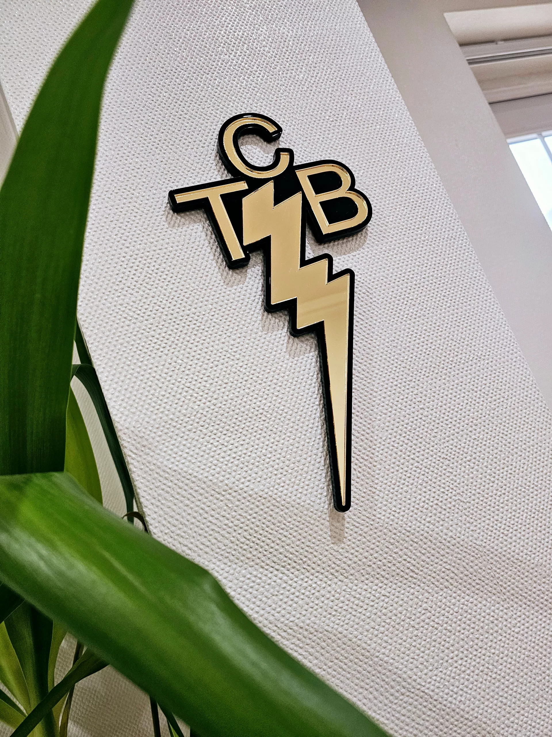 A piece of wall art made in the shape of the TCB necklace worn by Elvis Presley. Made with a black outline and mirror.