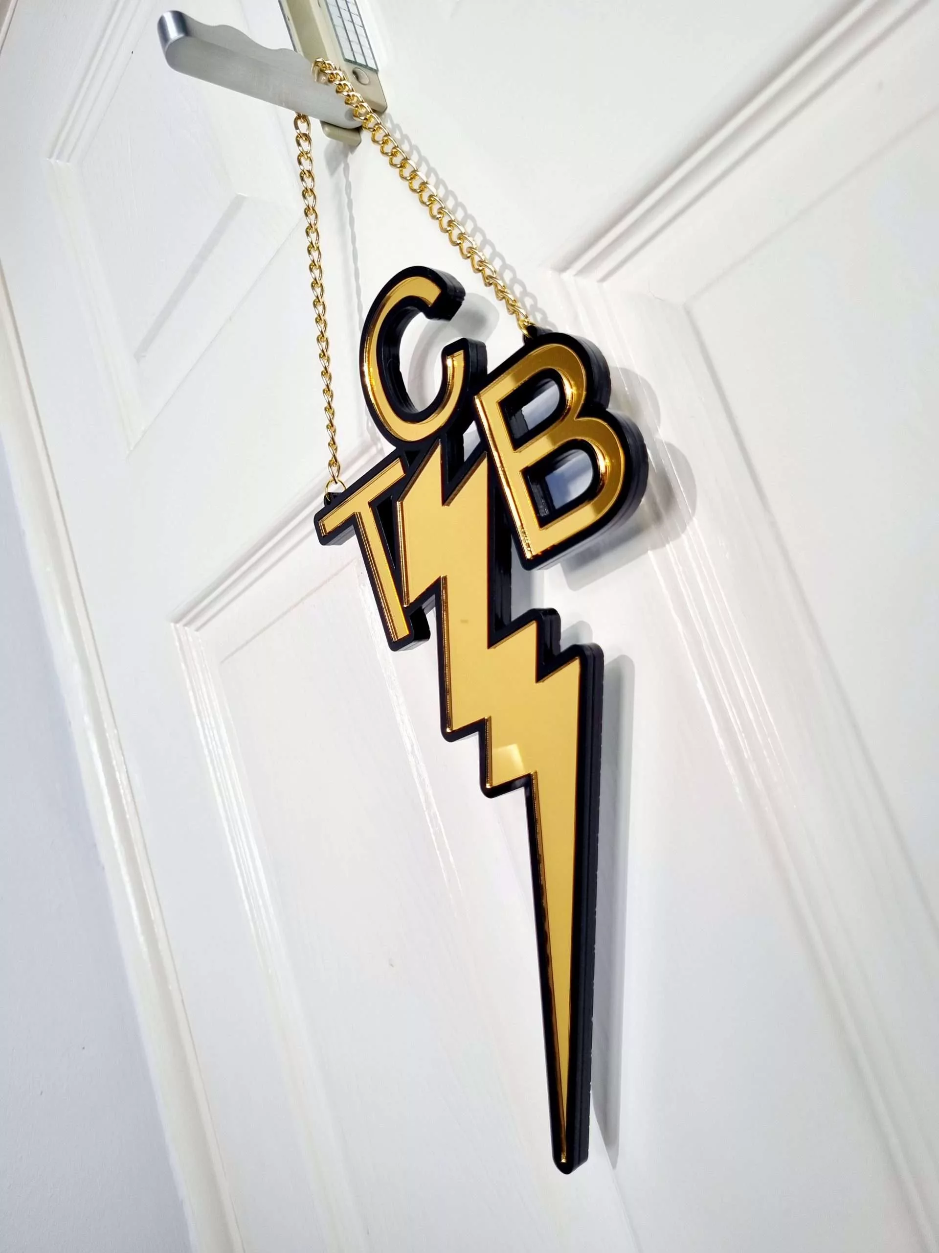 A handmade wall or door hanging in the style ofthe TCB necklace worn by Elvis Presley. The piece is gold with a black outline.