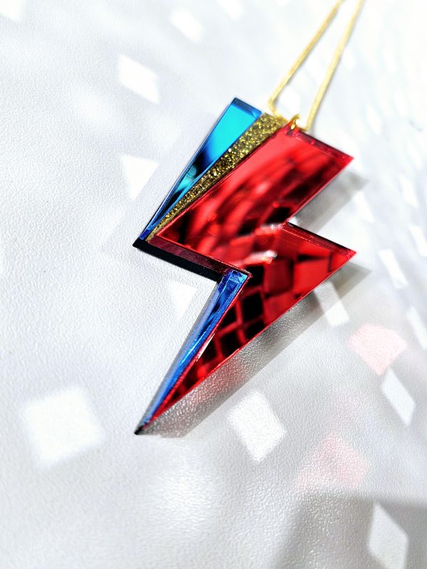 A pendant in the shape of a lightning bolt, made with red and blue mirrir acrylic, in the style of the iconic lightning bolt David Bowie worse across his face.