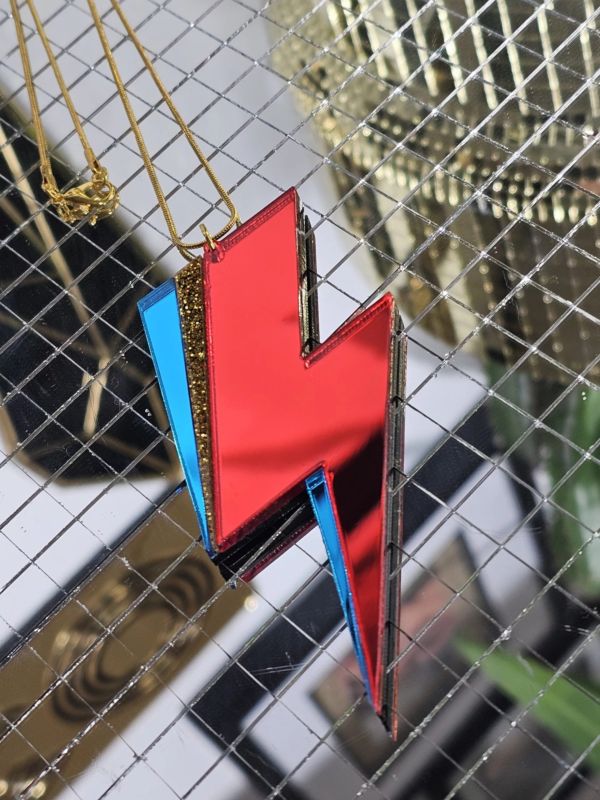A pendant in the shape of a lightning bolt, made with red and blue mirrir acrylic, in the style of the iconic lightning bolt David Bowie worse across his face.