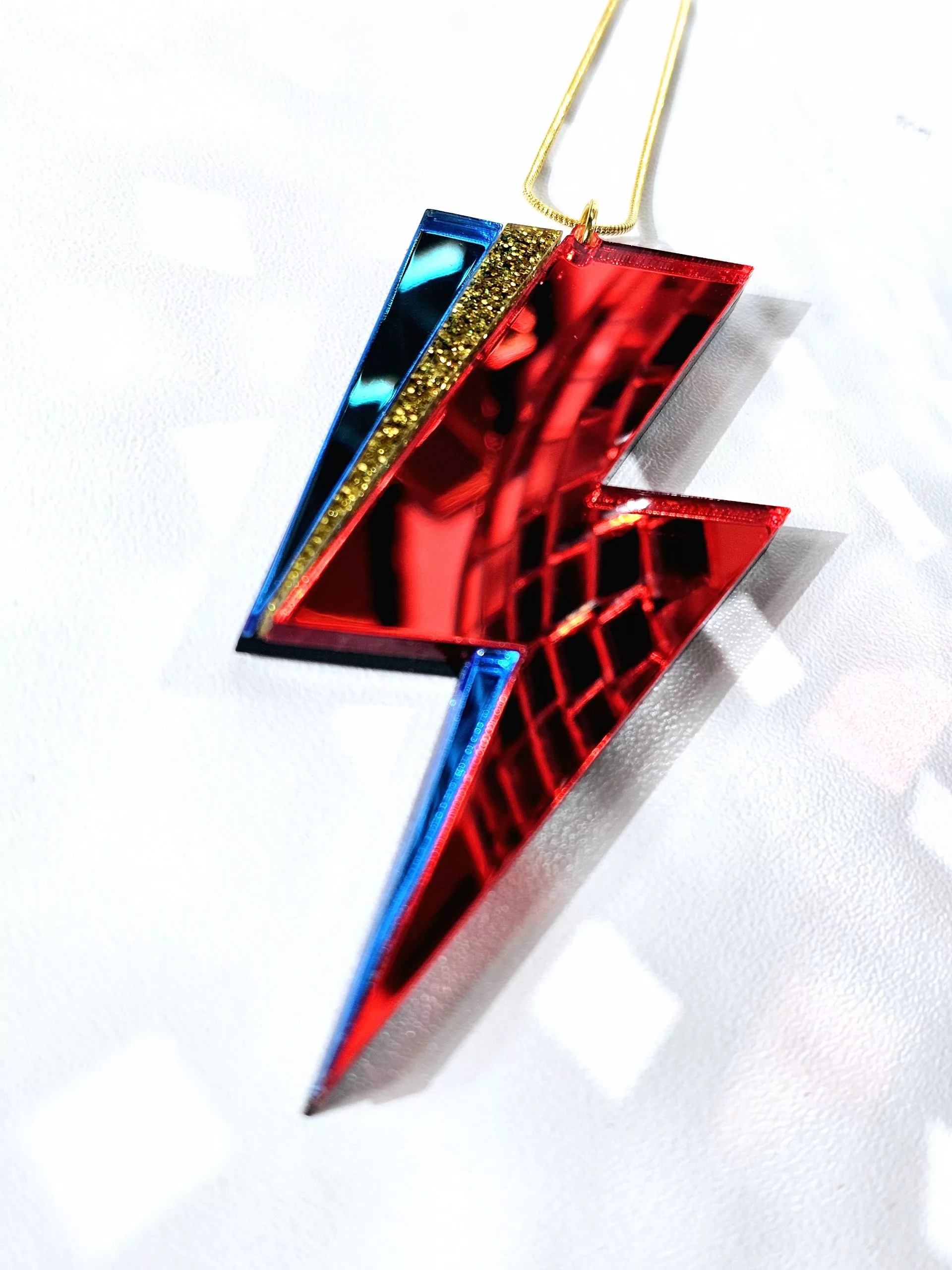 A pendant in the shape of a lightning bolt, made with red and blue mirrir acrylic, in the style of the iconic lightning bolt David Bowie worse across his face.