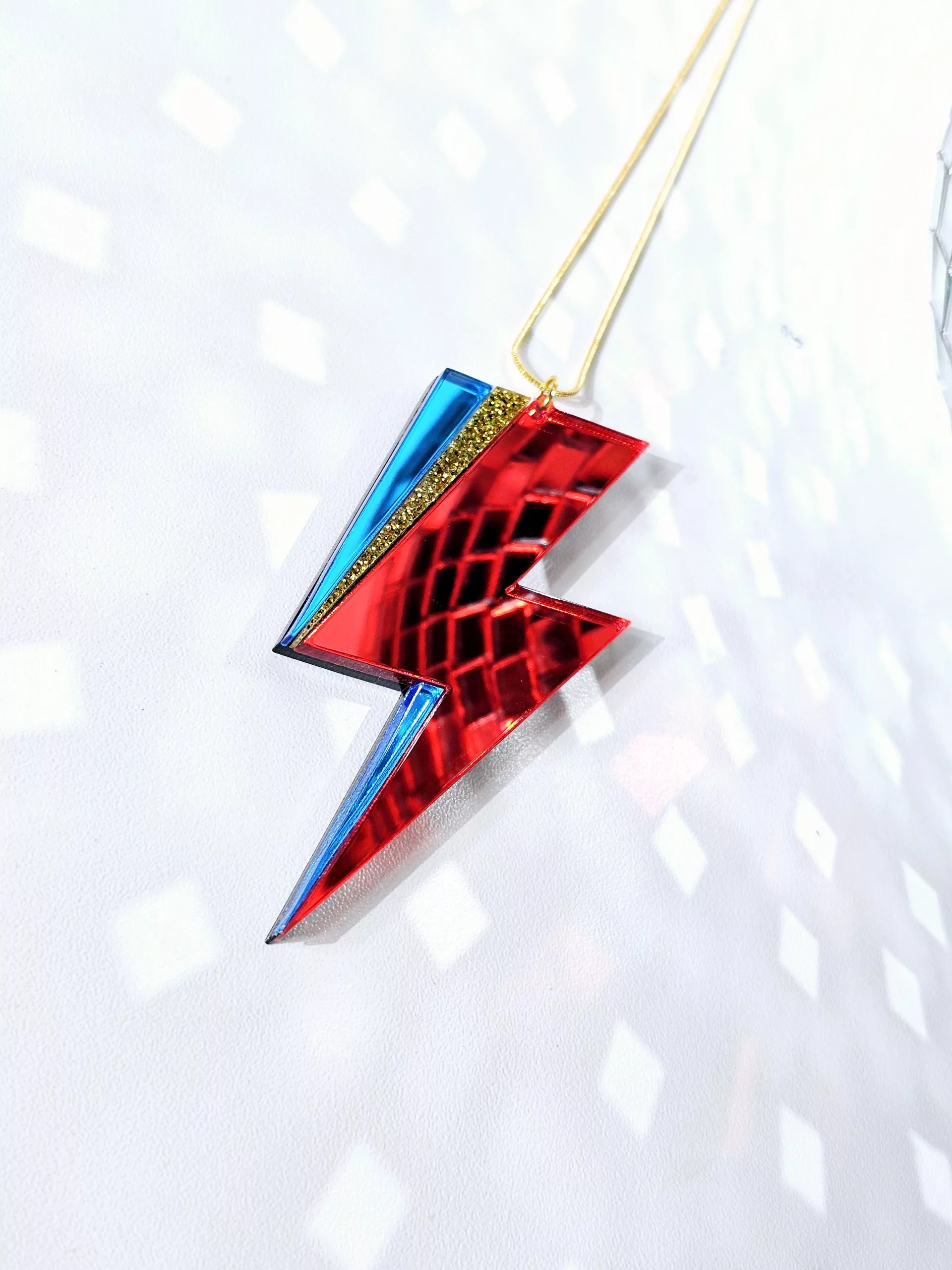 A pendant in the shape of a lightning bolt, made with red and blue mirrir acrylic, in the style of the iconic lightning bolt David Bowie worse across his face.