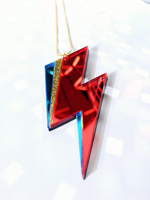 A pendant in the shape of a lightning bolt, made with red and blue mirrir acrylic, in the style of the iconic lightning bolt David Bowie worse across his face.
