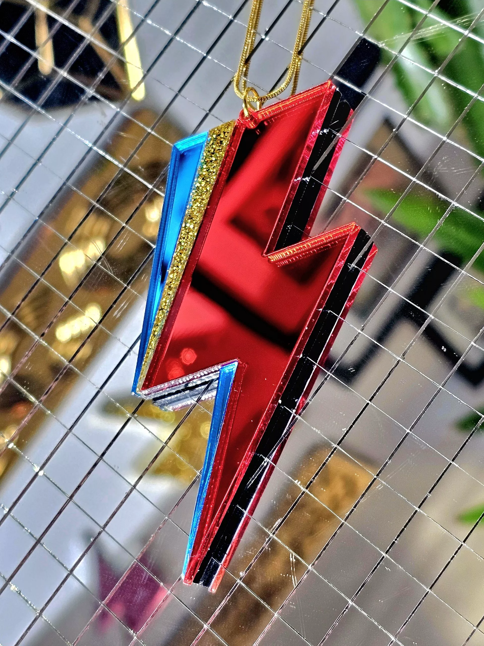 A pendant in the shape of a lightning bolt, made with red and blue mirrir acrylic, in the style of the iconic lightning bolt David Bowie worse across his face.