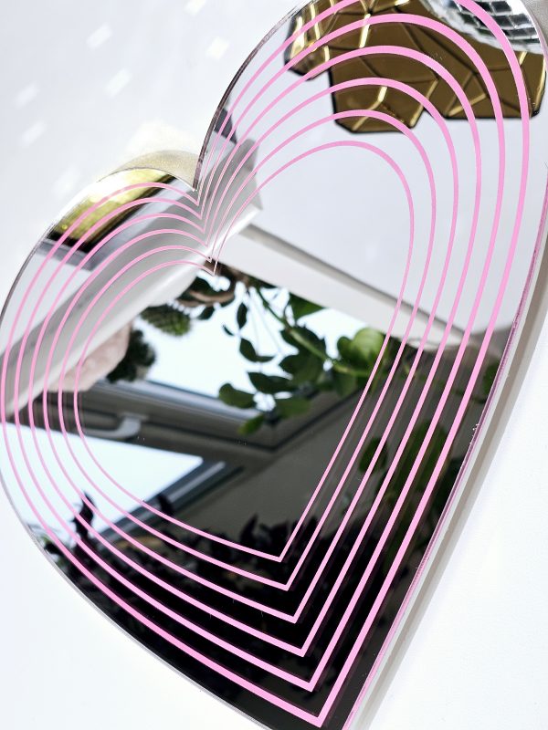 A silver mirror in the shape of a heart with pink hearts of decreasing sizes within it.