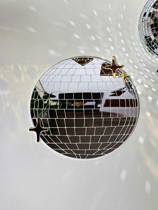 A handmade mirror in the shape of a disco ball. The mirror is silver with white lining and gold twinkles.