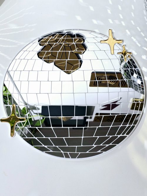 A handmade mirror in the shape of a disco ball. The mirror is silver with white lining and gold twinkles.