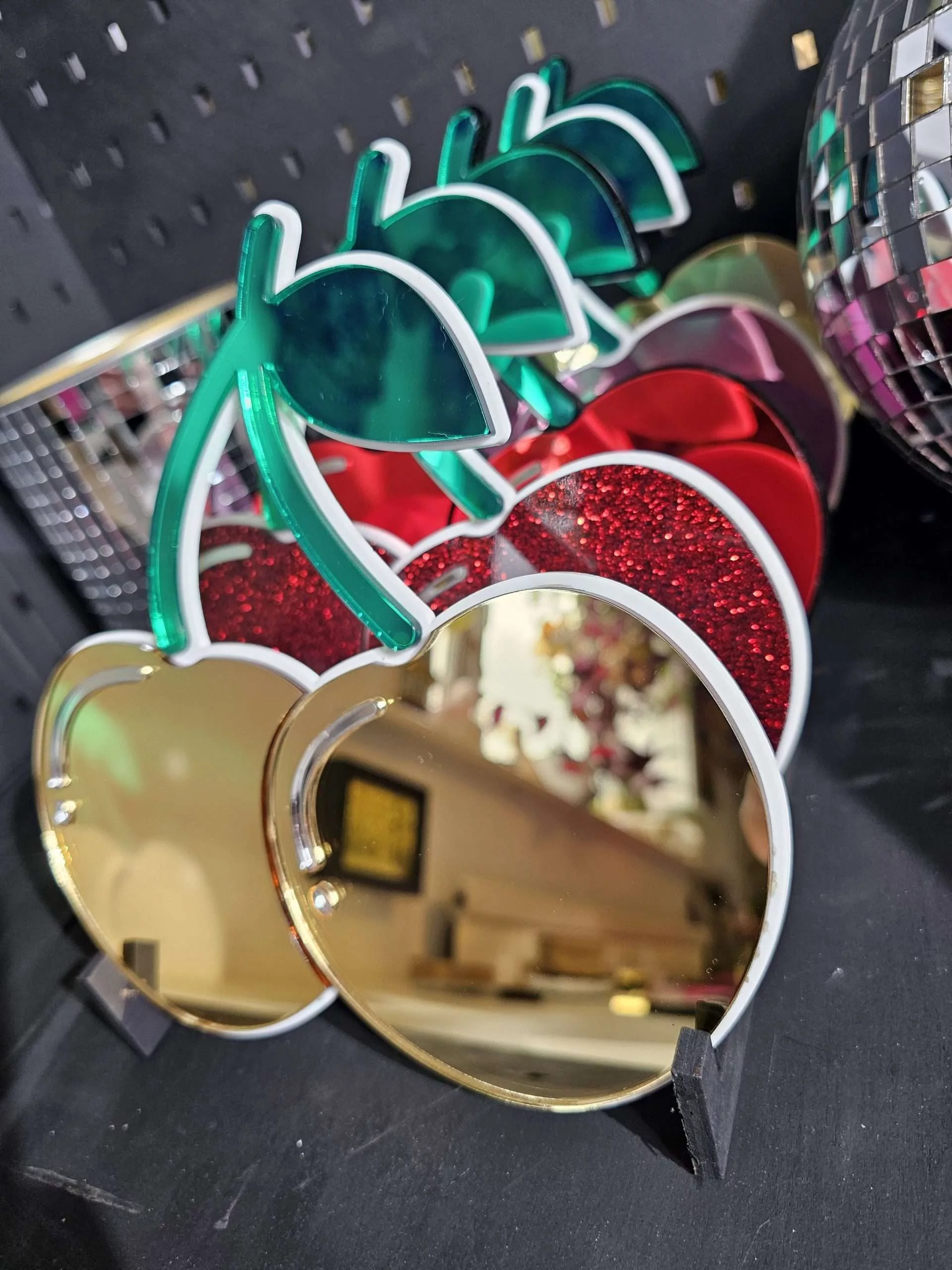 A row of cherry mirrors. The cherries are gold, red glitter and red with green leaves.