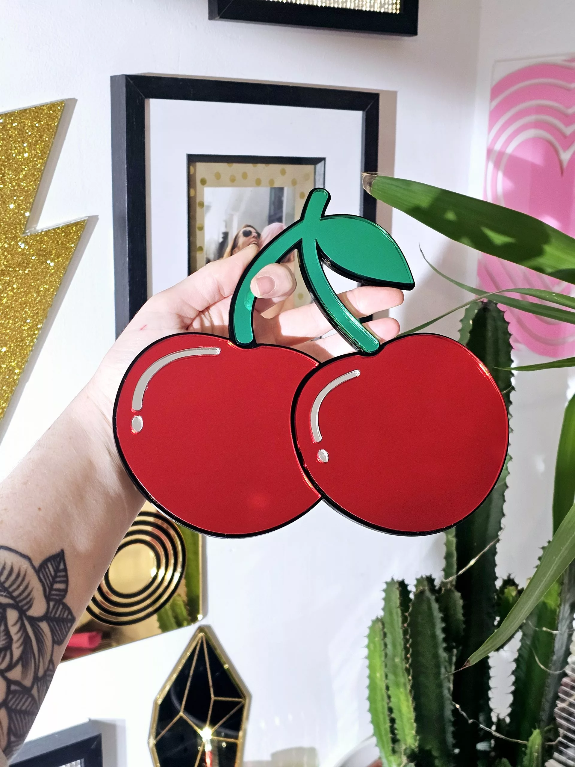 A handmade mirror in the shape of two heart shaped cherries with green mirror stem and leaves.