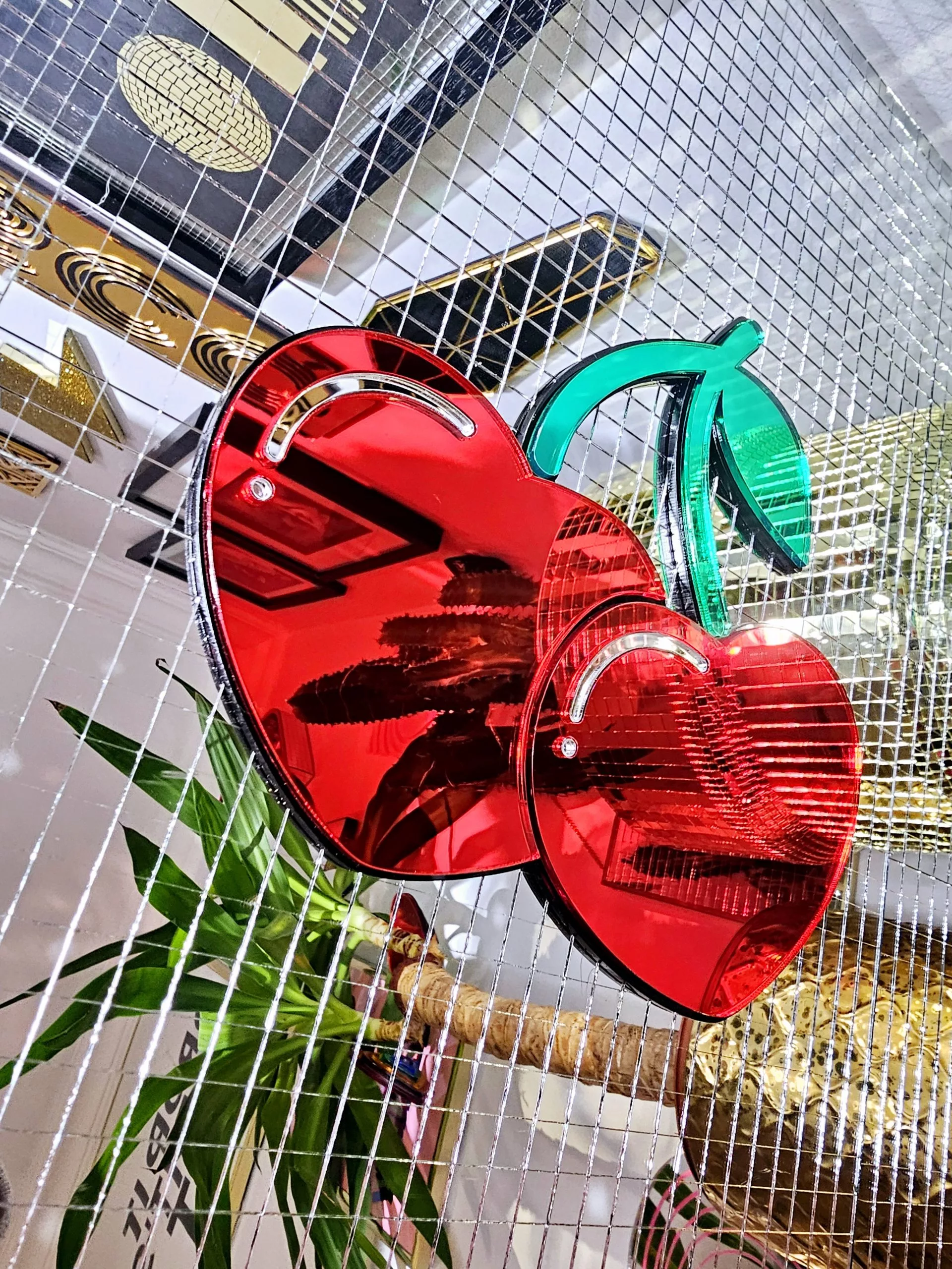 A handmade mirror in the shape of two heart shaped cherries with green mirror stem and leaves.