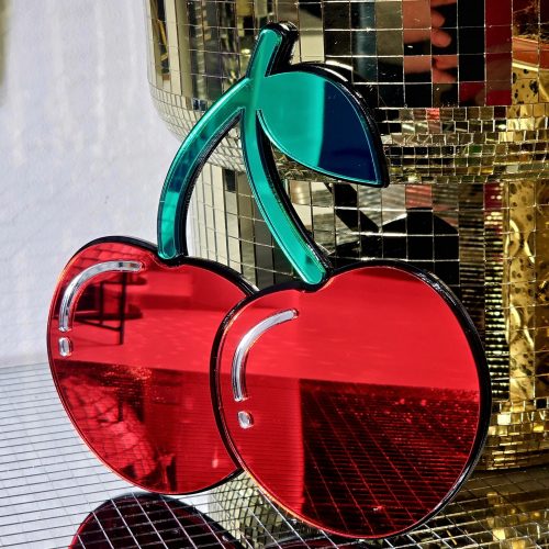 A handmade mirror in the shape of two heart shaped cherries with green mirror stem and leaves.