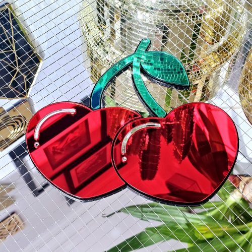 A handmade mirror in the shape of two heart shaped cherries with green mirror stem and leaves.