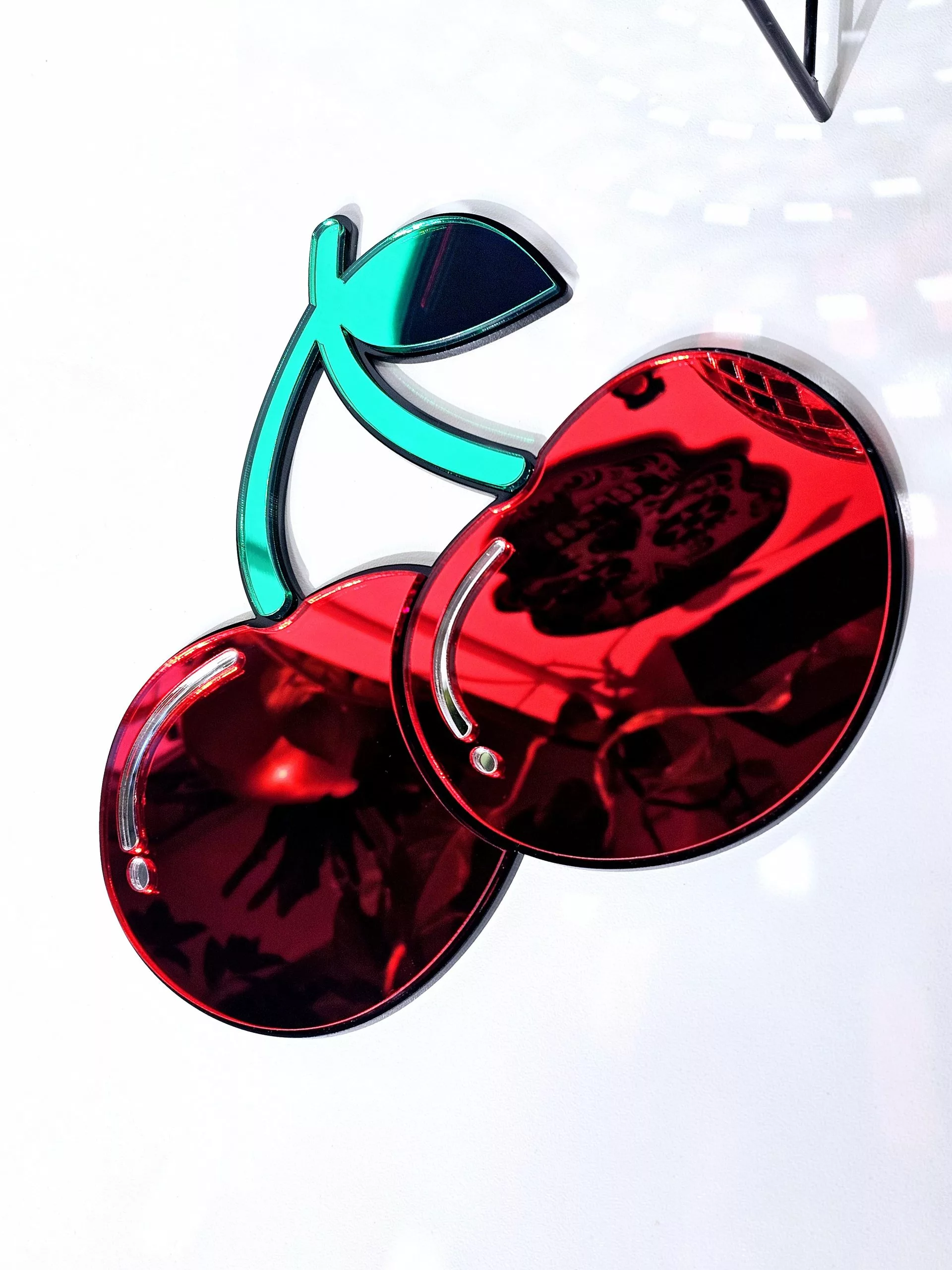 A handmade mirror in the shape of two heart shaped cherries with green mirror stem and leaves.