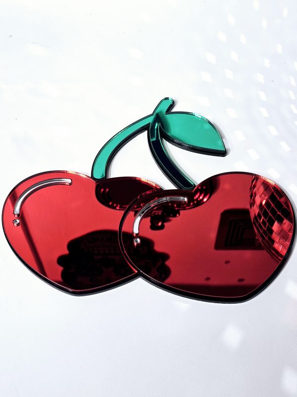A handmade mirror in the shape of two heart shaped cherries with green mirror stem and leaves.