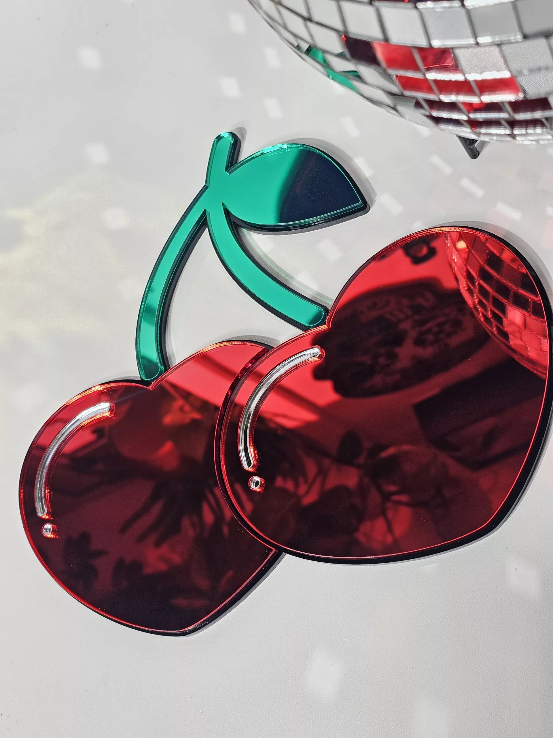 A handmade mirror in the shape of two heart shaped cherries with green mirror stem and leaves.
