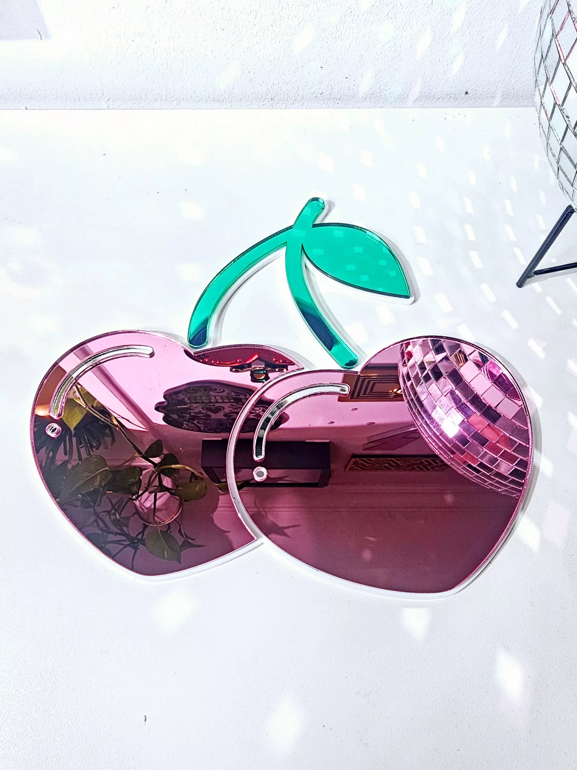 A handmade mirror in the shape of two heart shaped cherries with green mirror stem and leaves.