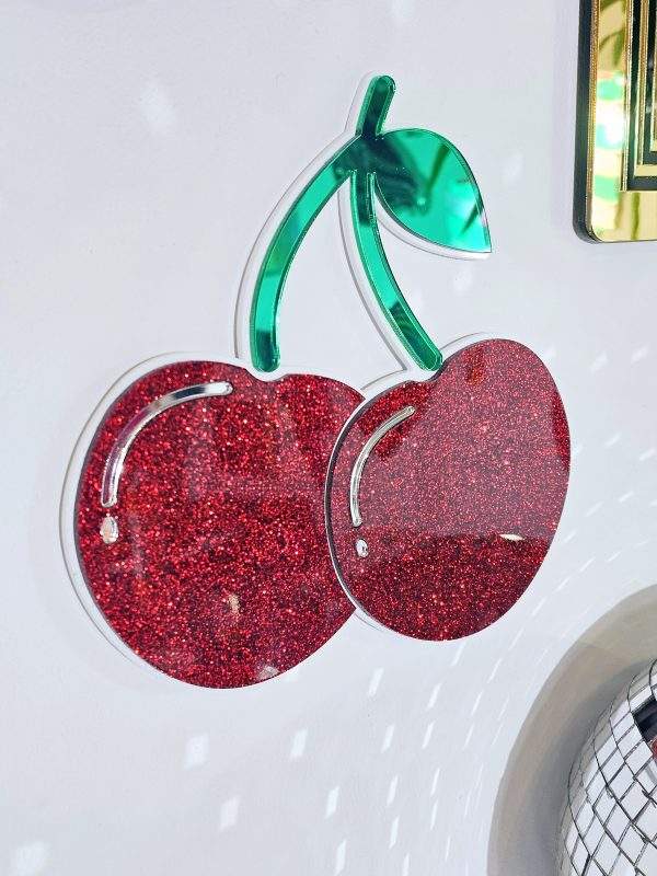 A handmade mirror in the shape of cherries. The cherries are red glitter with a white outline,
