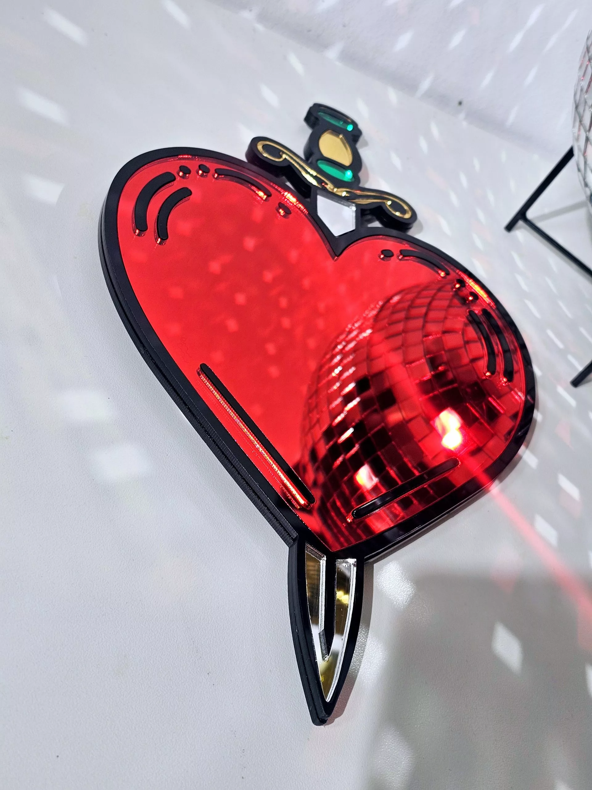 A handmade mirror in the shape of a heart and dagger, in an old school tattoo style. The heart is red with a black outline and orgate dagger design.