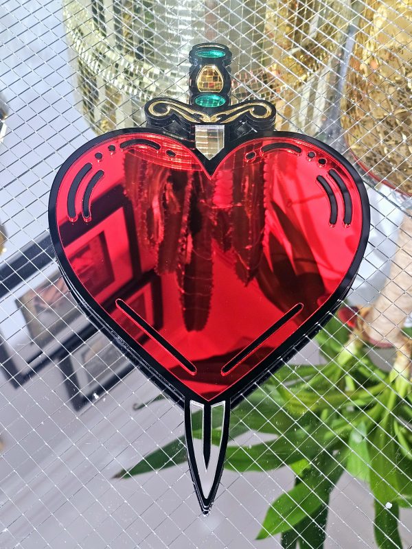 A handmade mirror in the shape of a heart and dagger, in an old school tattoo style. The heart is red with a black outline and orgate dagger design.