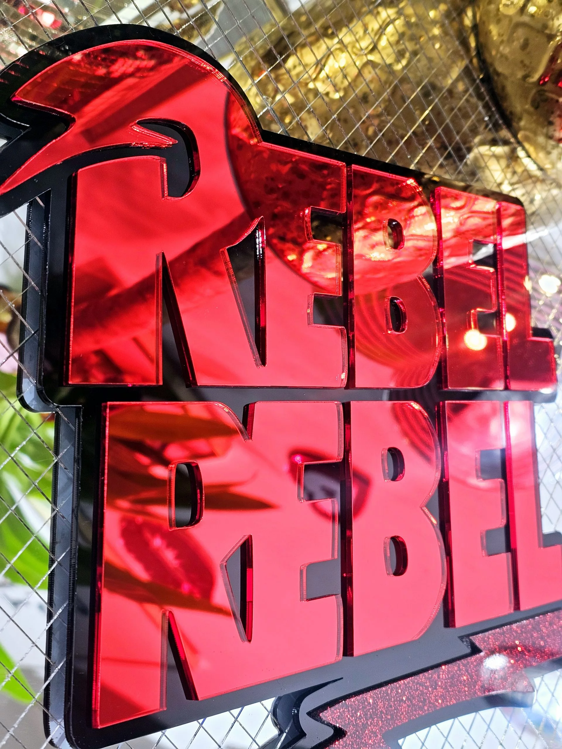 A piece of wall art with the text Rebel Rebel in red mirror with a black background.