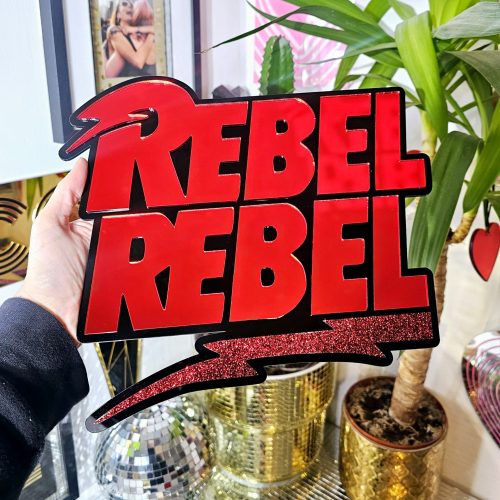 A piece of wall art with the text Rebel Rebel in red mirror with a black background.