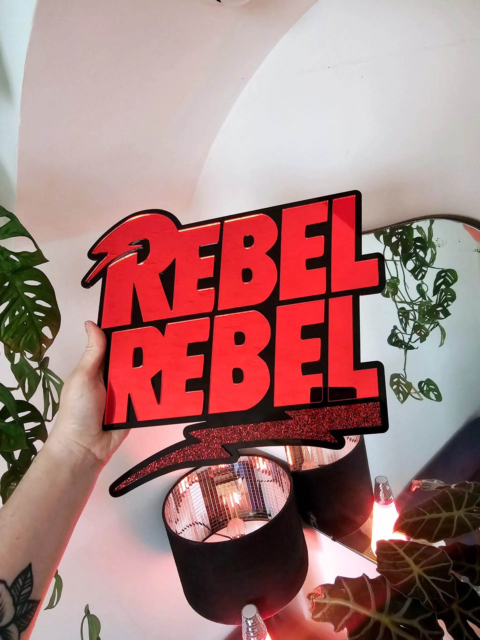 A piece of wall art with the text Rebel Rebel in red mirror with a black background.