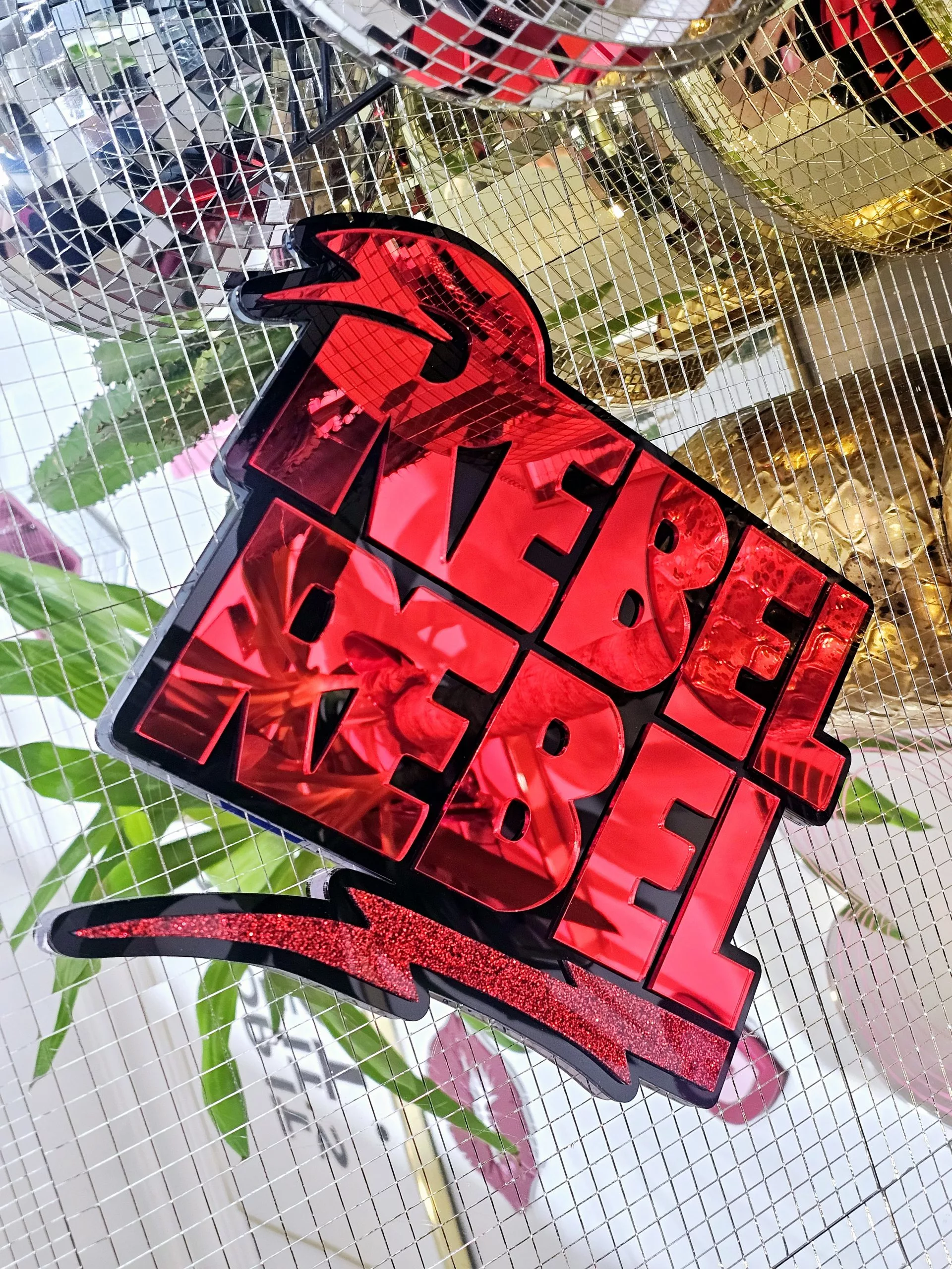 A piece of wall art with the text Rebel Rebel in red mirror with a black background.