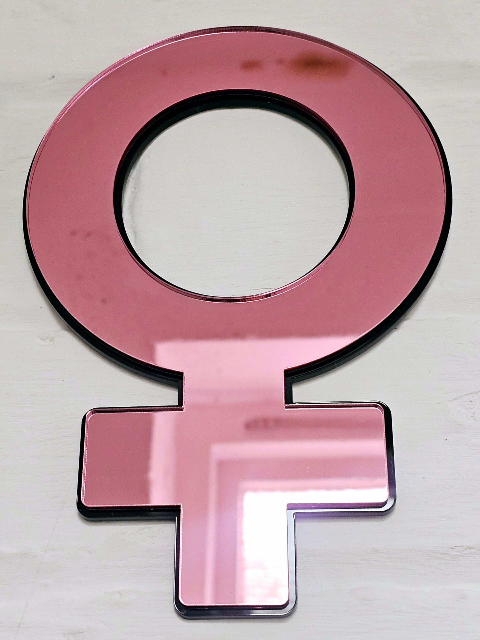 The female symbol made from pink mirror with a black backing. Mounted on a white brick wall.