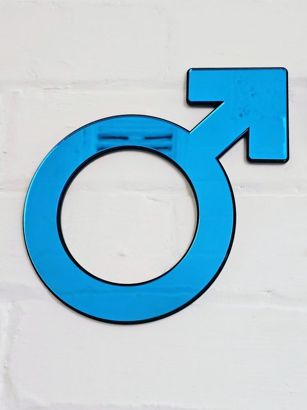 The male symbol made from blue mirror with a black backing. Mounted on a white brick wall.